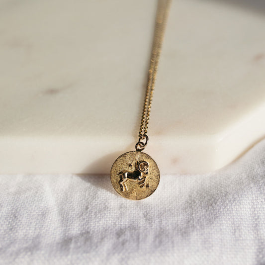 Close-up of a round gold zodiac pendant showing its astrological symbol and textured matte finish.