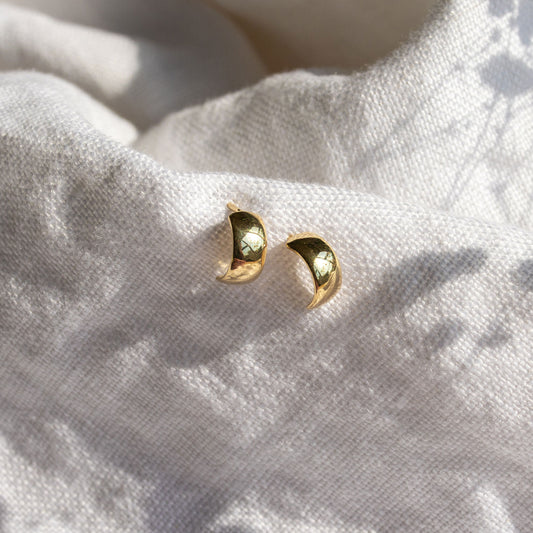 Mini yellow gold bold stud earrings displayed on soft textured fabric.