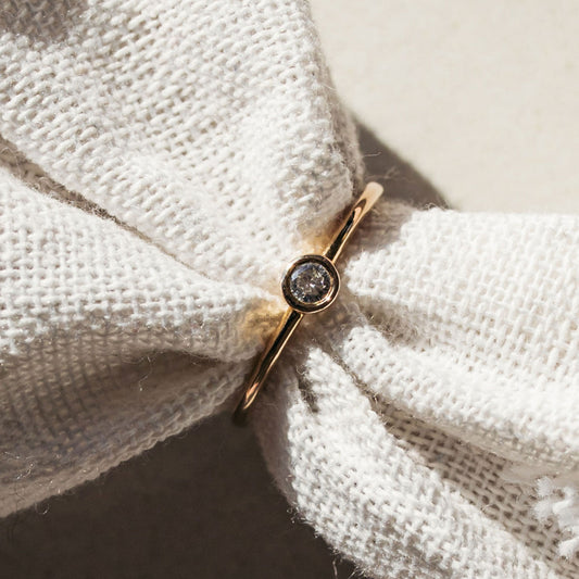 Close-up of a single diamond ring in a 9ct gold setting, photographed on textured fabric.