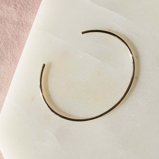 Close-up of a slim oval gold cuff bracelet showcasing its smooth, minimalist open-ended design.
