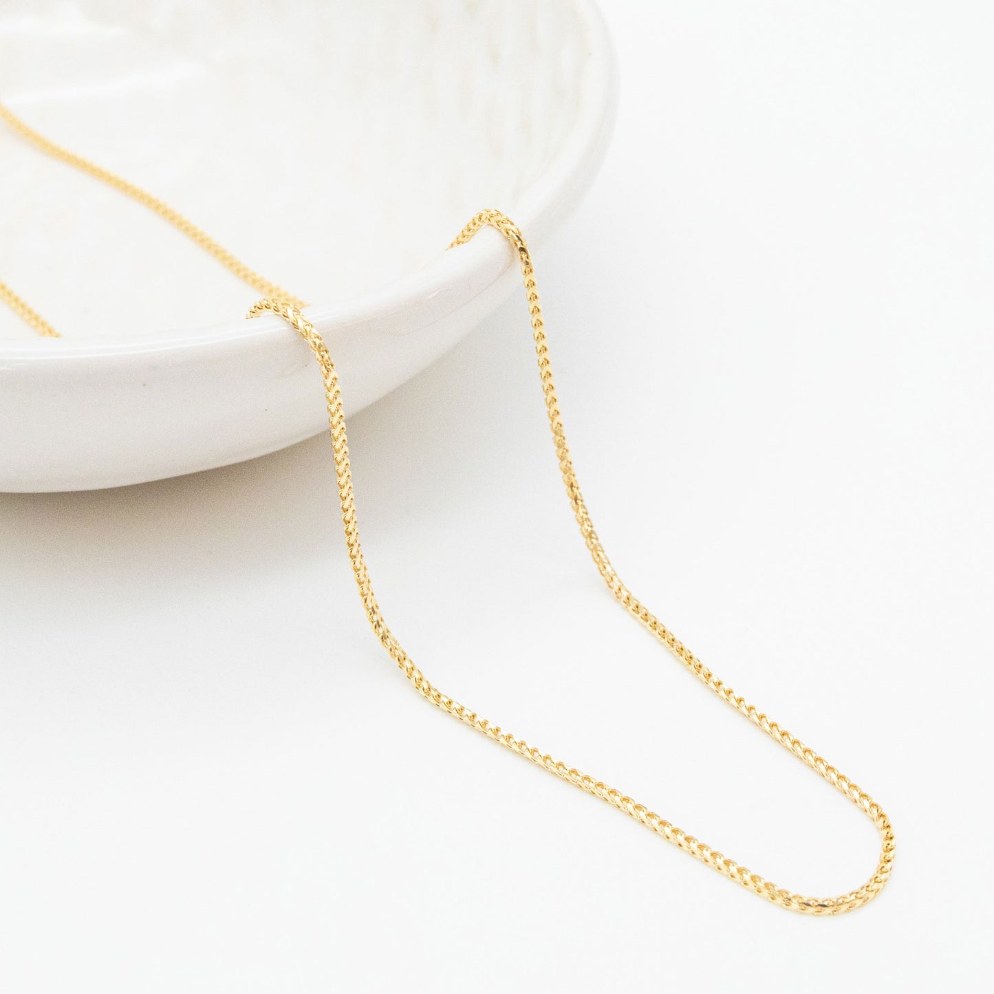 9ct yellow gold 1.1mm Franco chain necklace draped over a white ceramic dish