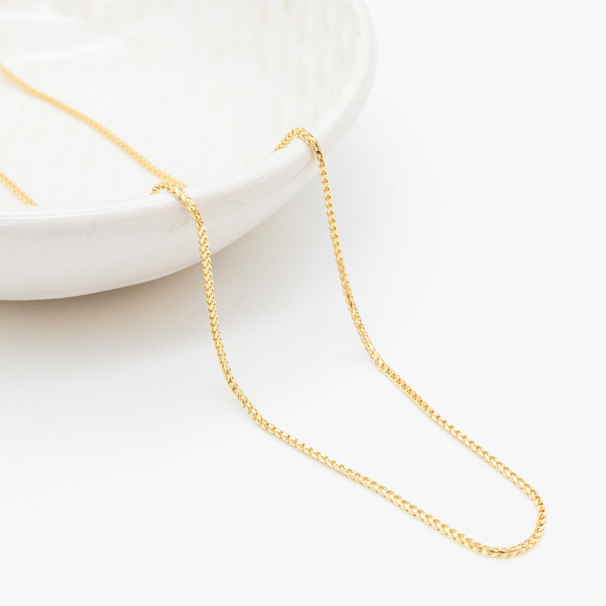9ct yellow gold 1.1mm Franco chain necklace draped over a white ceramic dish