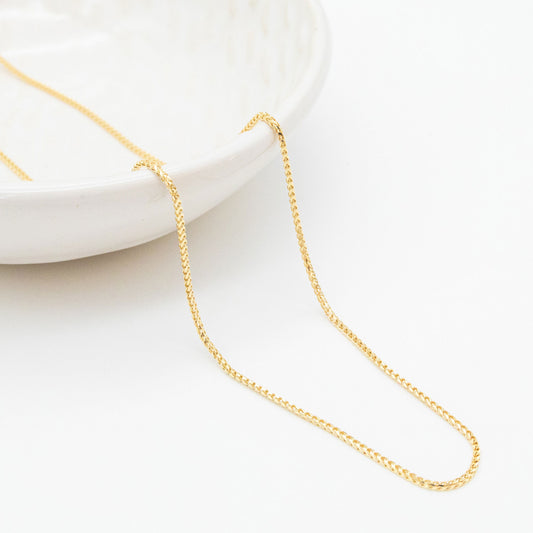 9ct yellow gold 1.1mm Franco chain necklace draped over a white ceramic dish