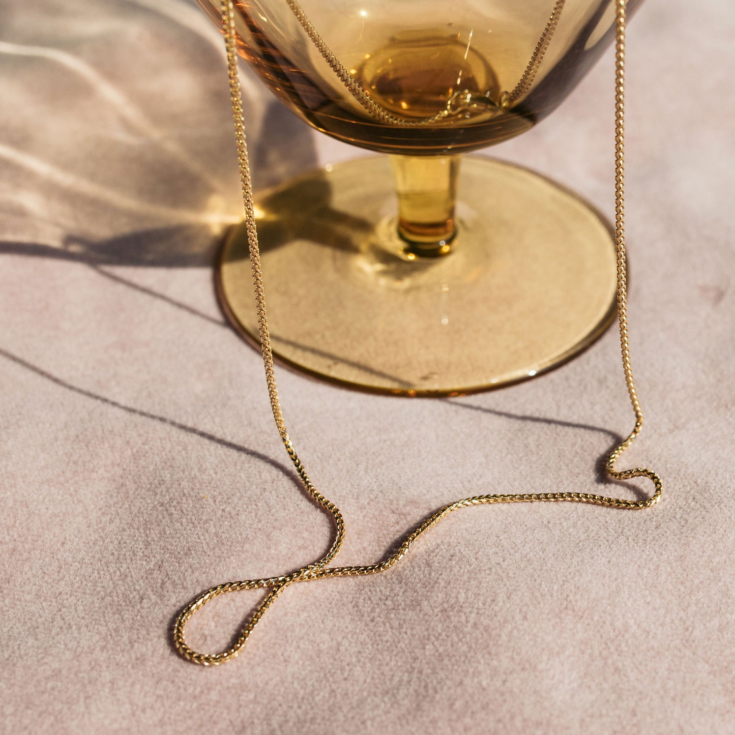 9ct yellow gold 1.1mm Franco chain necklace draped over a glass tumbler