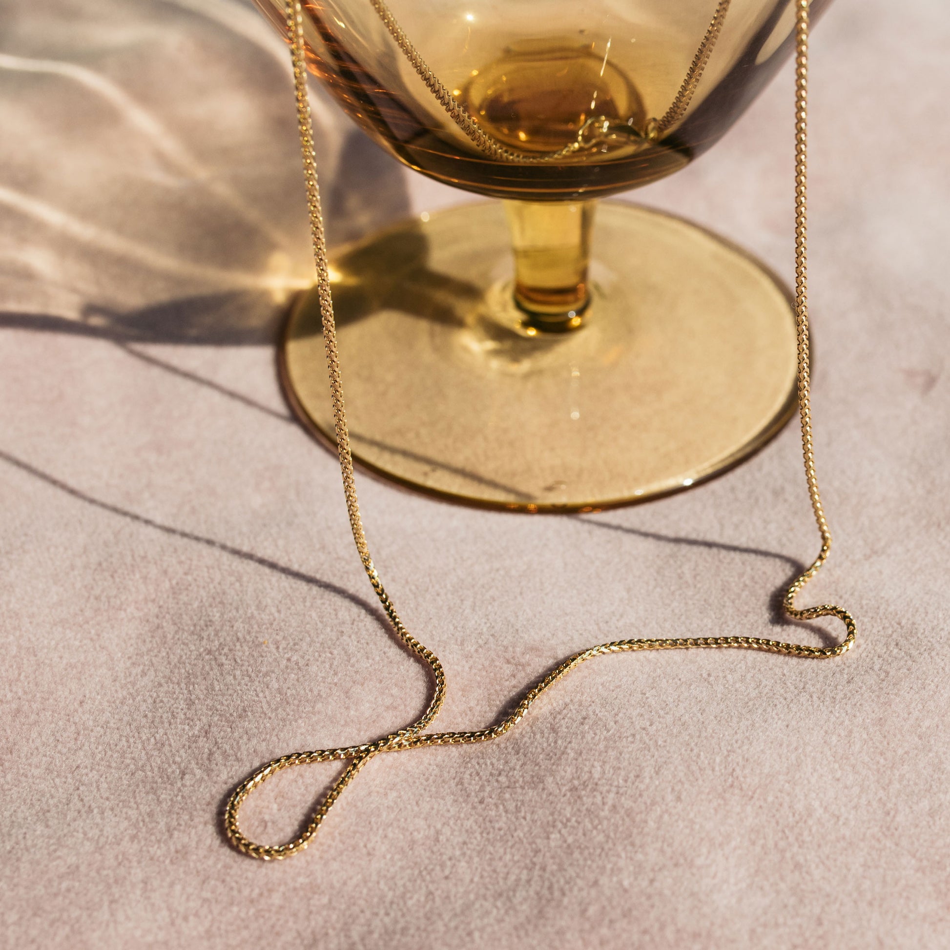 9ct yellow gold 1.1mm Franco chain necklace draped over a glass tumbler