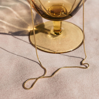 9ct yellow gold 1.1mm Franco chain necklace draped over a glass tumbler