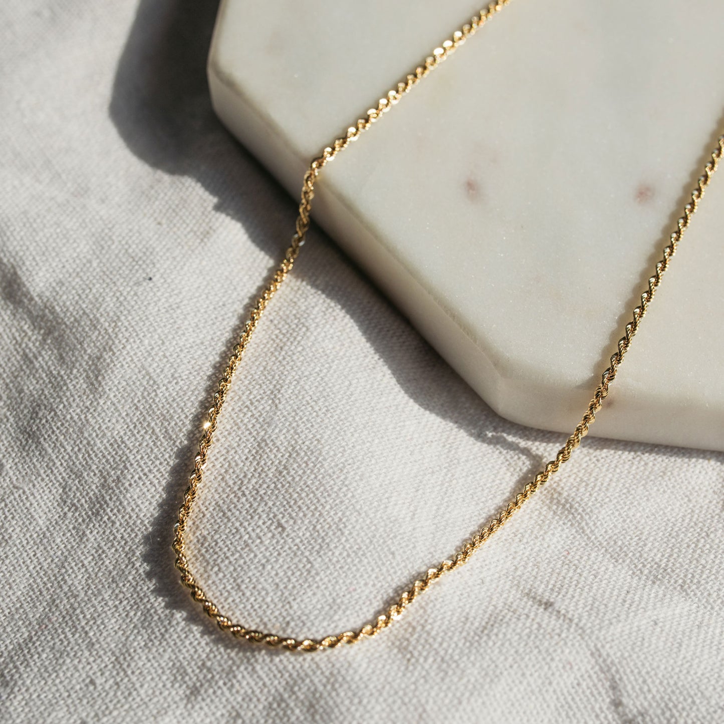 A 9ct yellow gold rope chain necklace laid out on a white surface.