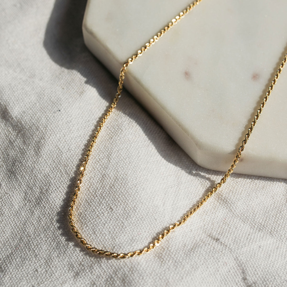 A 9ct yellow gold rope chain necklace laid out on a white surface.