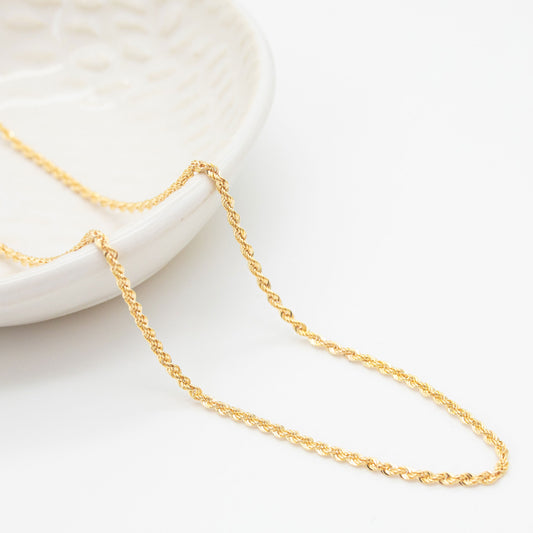 A 9ct yellow gold rope chain necklace laid out on a white surface.