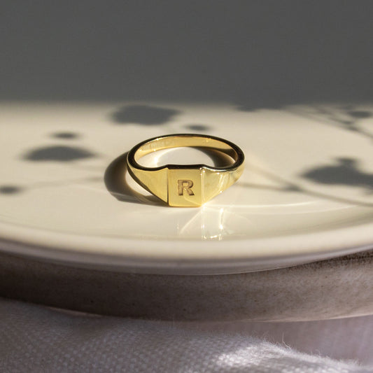 Close-up of a 9ct gold pinky signet ring showcasing its engraved initial and polished gold finish.