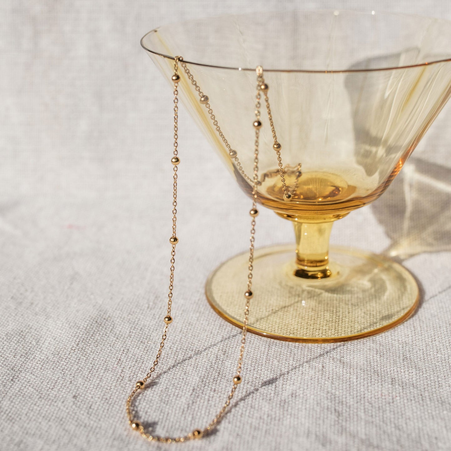 A delicate gold chain necklace with evenly spaced small gold beads, draped elegantly over a yellow tumbler