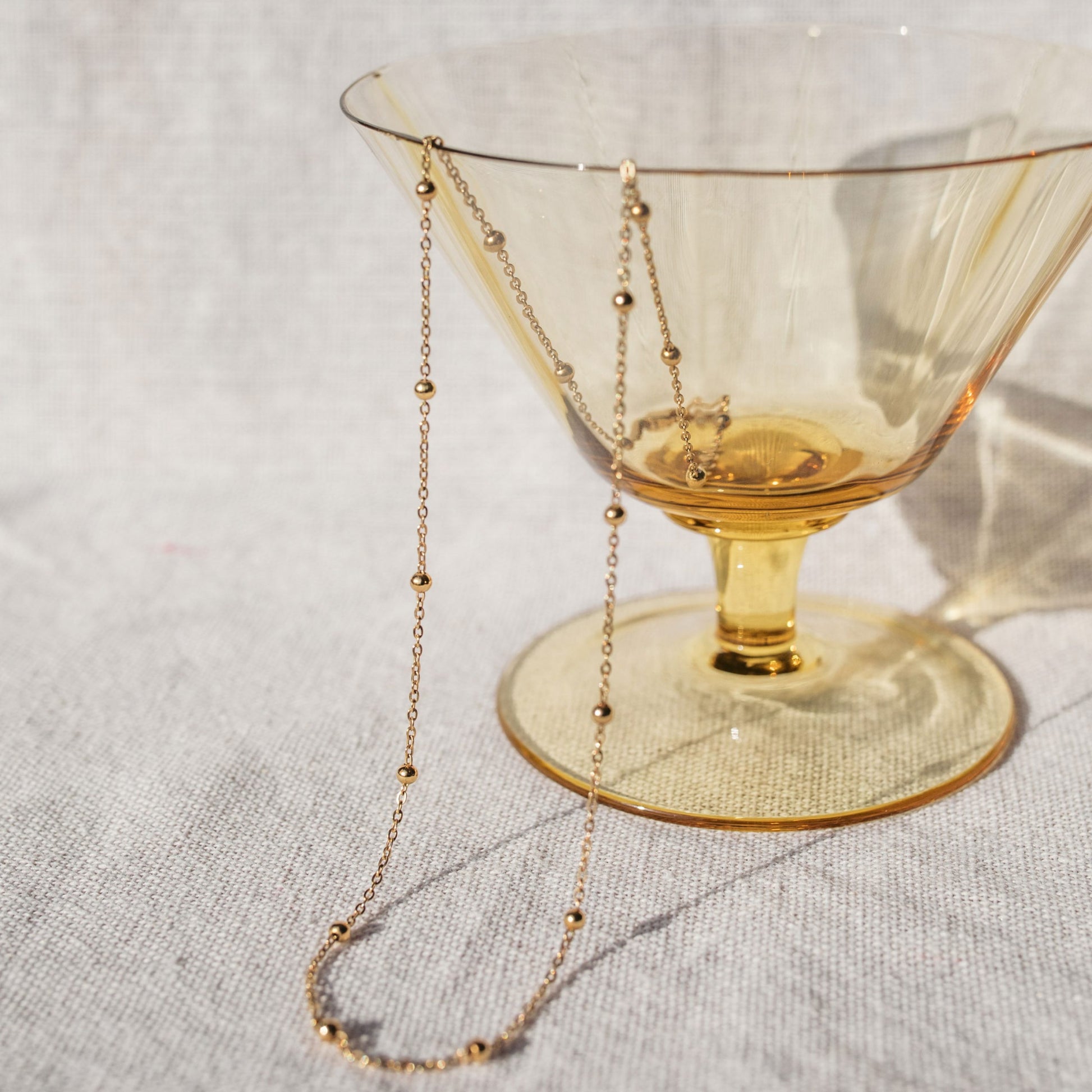 A delicate gold chain necklace with evenly spaced small gold beads, draped elegantly over a yellow tumbler