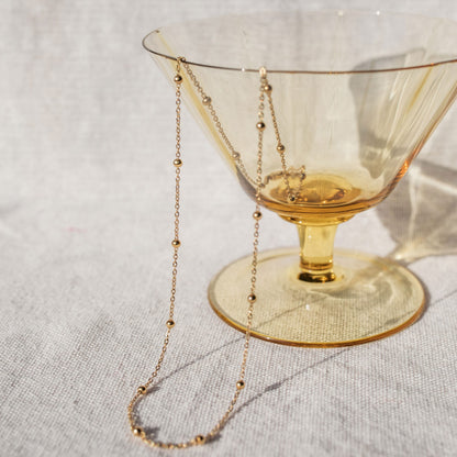 A delicate gold chain necklace with evenly spaced small gold beads, draped elegantly over a yellow tumbler