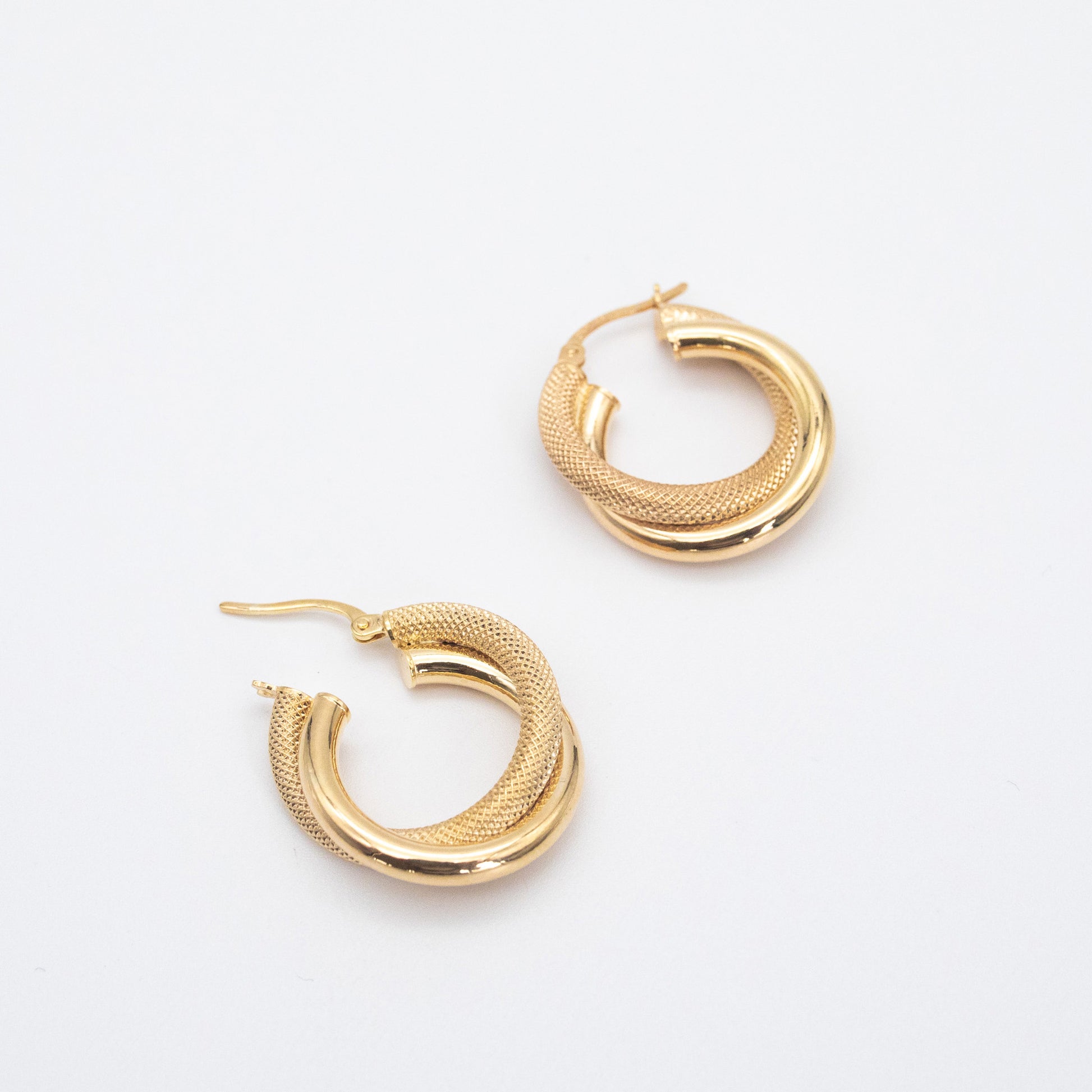 Double tube twisted hollow gold hoop earrings on white background.