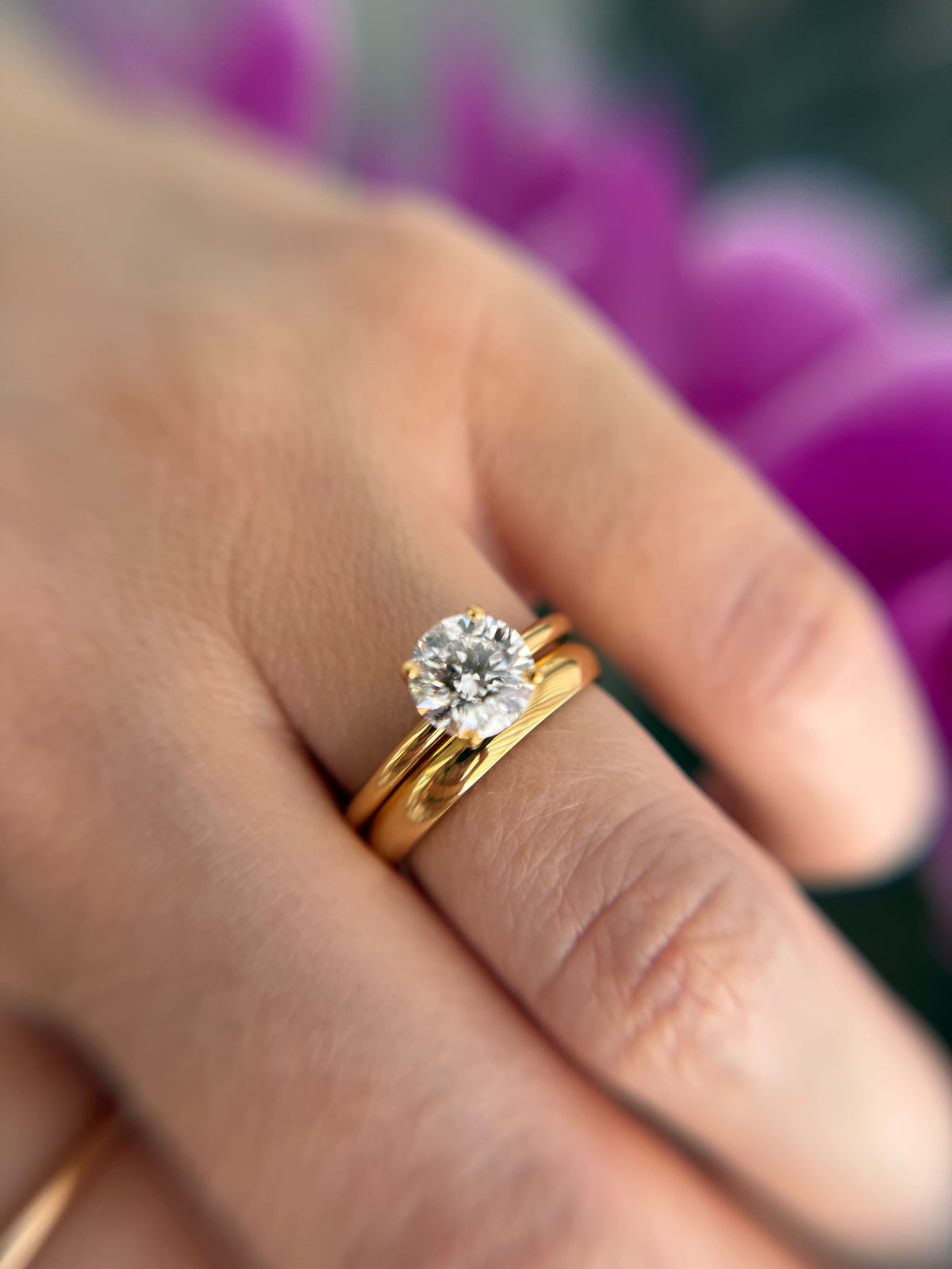 Round brilliant-cut diamond engagement ring in yellow gold with a matching diamond band, worn on a hand