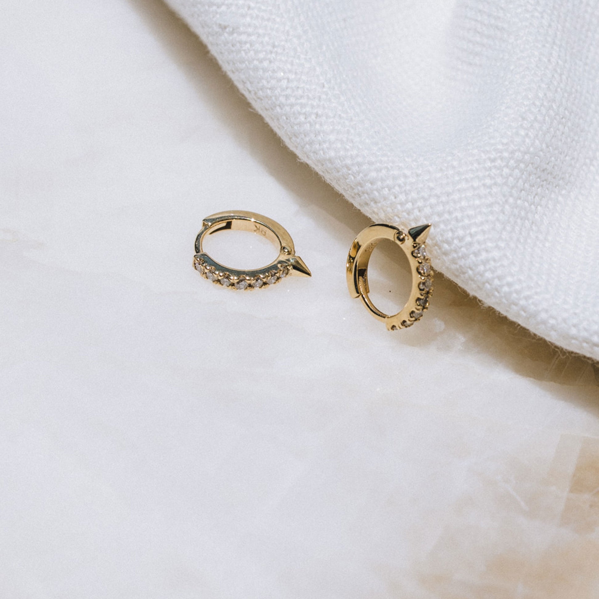 Pair of 9ct gold Spike Diamond Huggie earrings displayed on white background, showcasing front-facing diamonds.