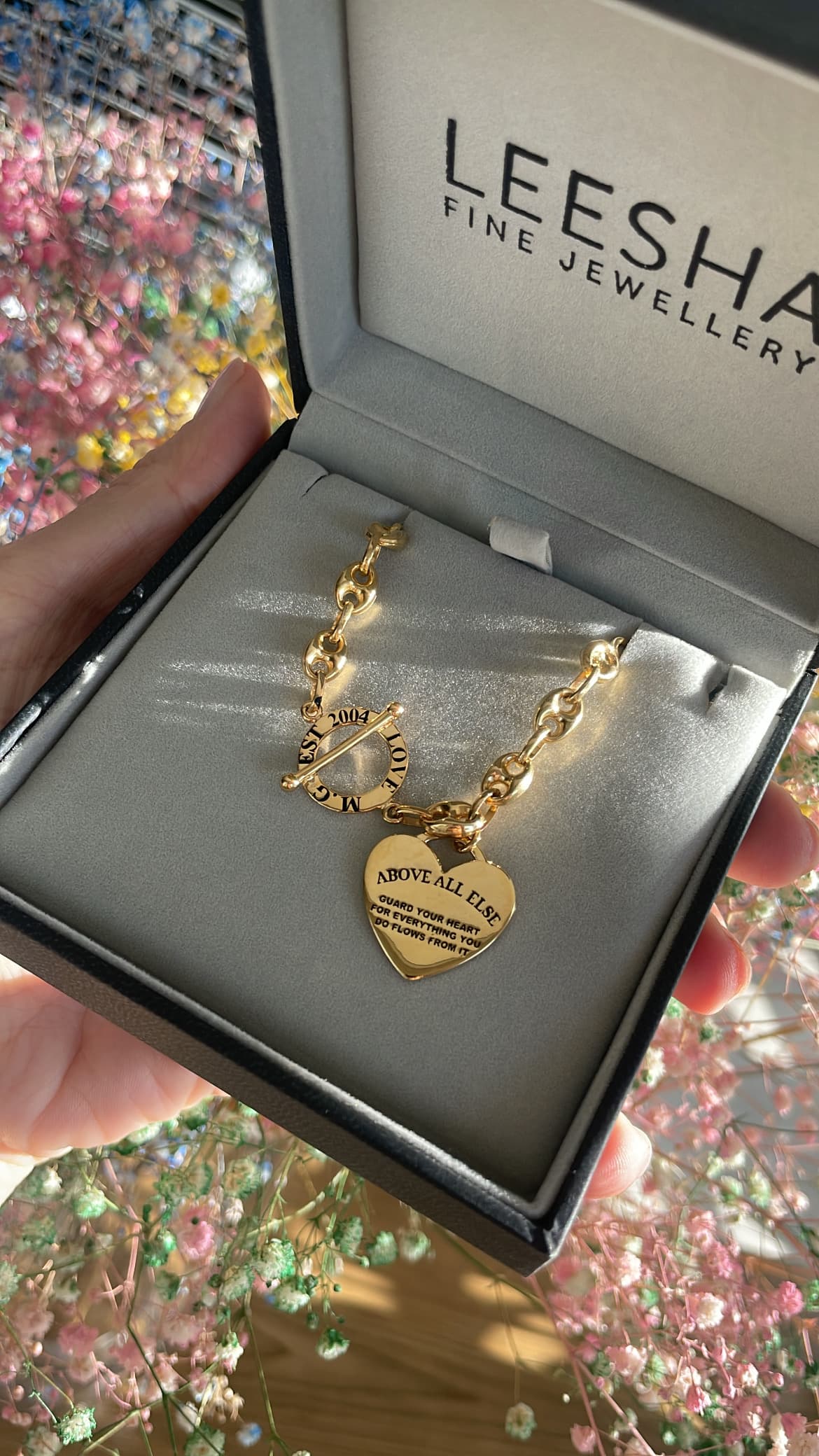 Custom yellow gold statement link bracelet featuring an engraved heart-shaped charm with scripture quote and a decorative toggle clasp, presented in an open black LEESHA Fine Jewellery gift box