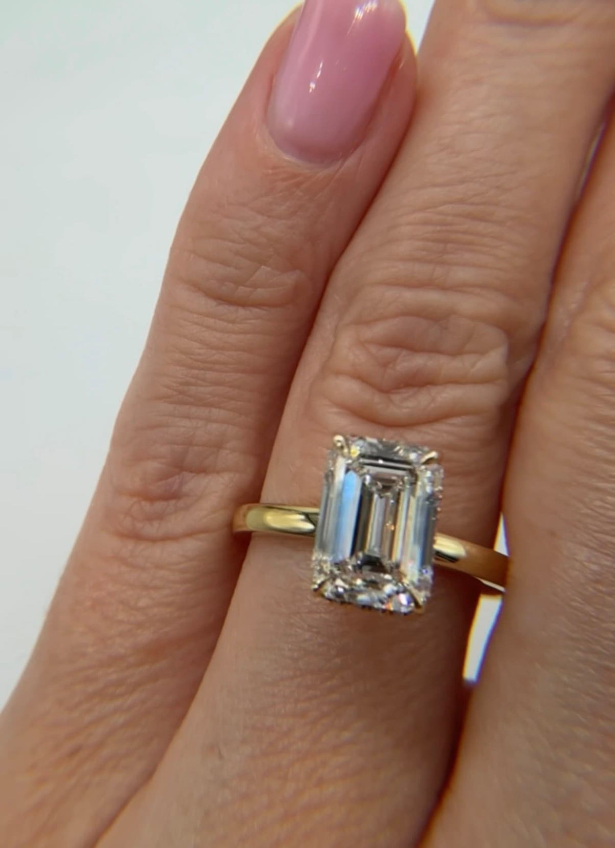 Emerald-cut diamond engagement ring in yellow gold with a delicate diamond halo worn on a hand