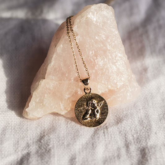 Close-up of a guardian angel pendant necklace showing the raised angel design and lightly hammered gold background.