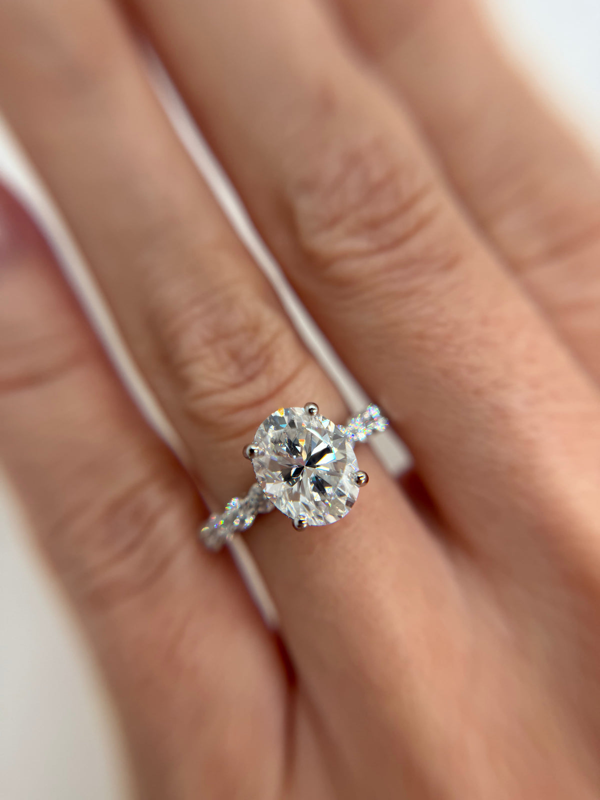 A close-up of a diamond engagement ring with a oval-cut center stone and a pavé band, worn on a hand.