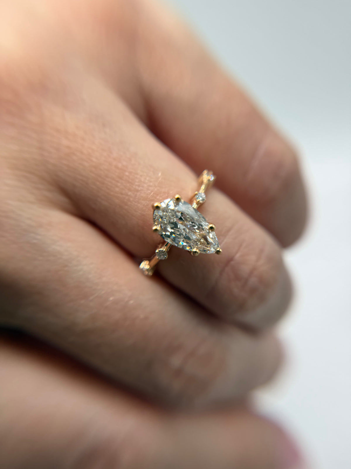Pear-shaped diamond engagement ring in yellow gold with diamond-set accents on the band, worn on a hand