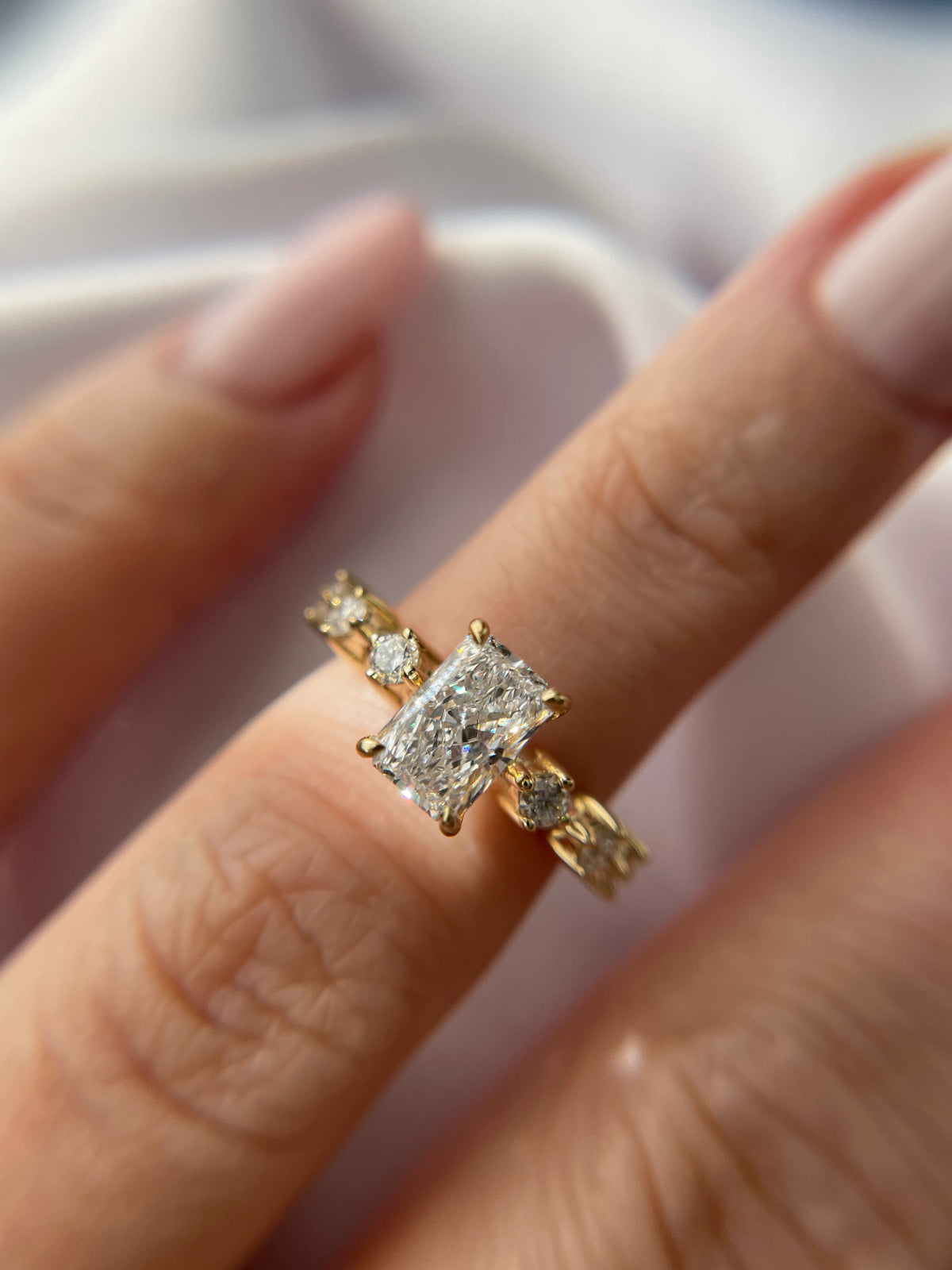 Radiant-cut diamond engagement ring in yellow gold with diamond accent stones on the band, worn on a hand
