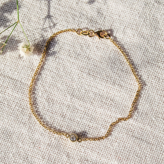 Delicate 9ct yellow gold single diamond bracelet arranged on a textured neutral surface.