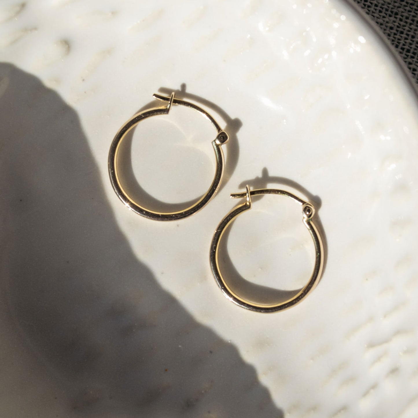 Close-up of 9ct gold small hoops highlighting polished shine and V-clip closure.