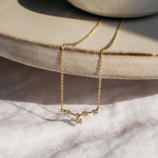 Close-up of a delicate gold zodiac necklace featuring a small diamond-set star sign pendant.